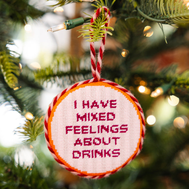 Decorative ornament with text 'I have mixed feelings about drinks' hanging on a Christmas tree.