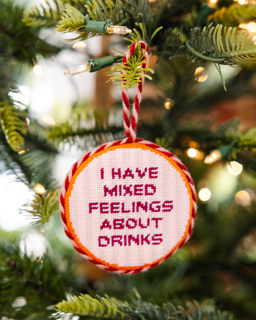 Decorative ornament with text 'I have mixed feelings about drinks' hanging on a Christmas tree.