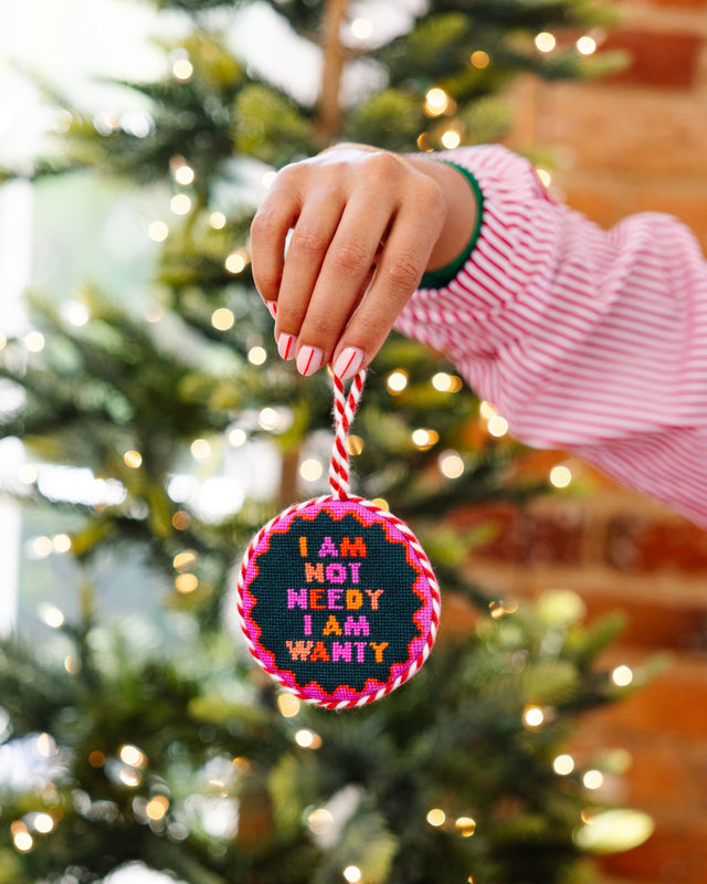 Person holding a colorful ornament with text in front of a Christmas tree