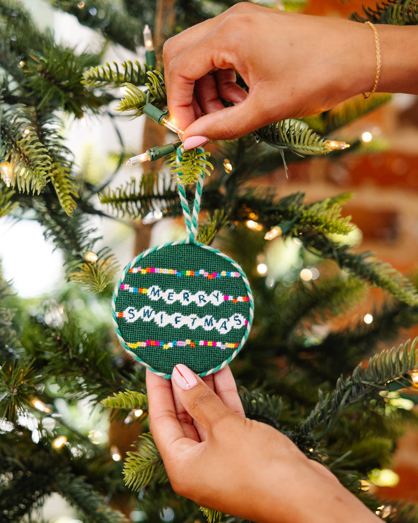 Hand holding a festive ornament with 'Merry Swiffermas' text on a decorated Christmas tree.