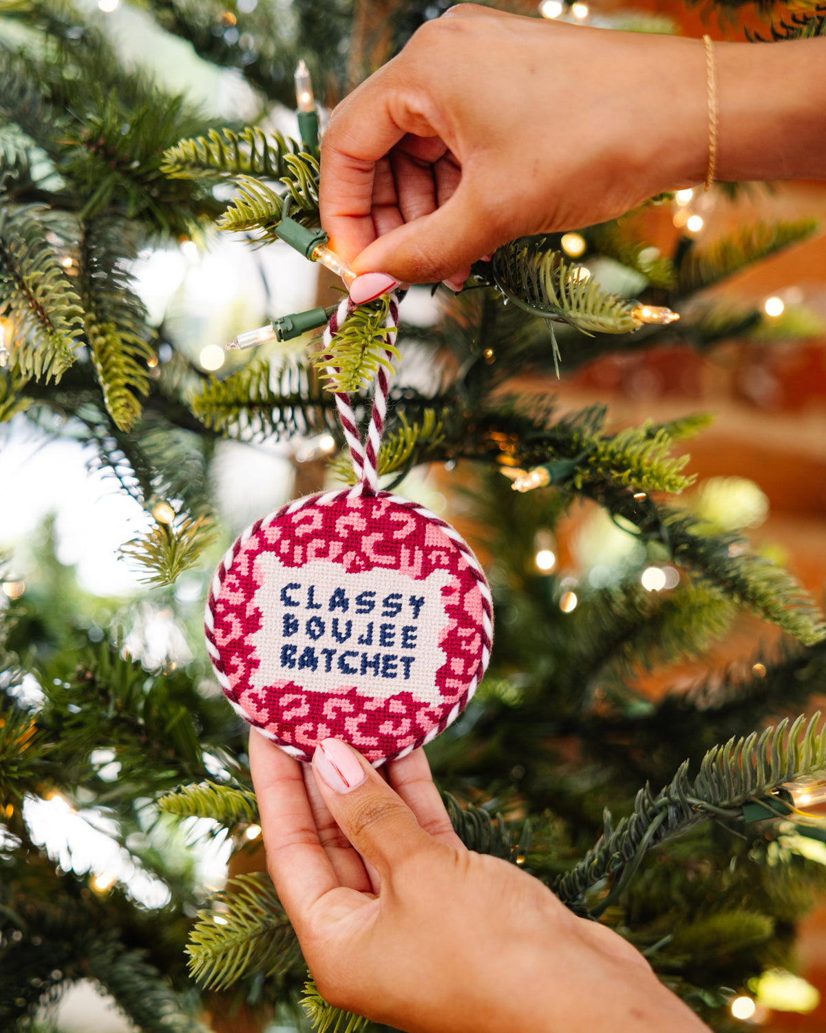Person holding a decorative ornament with text on a Christmas tree