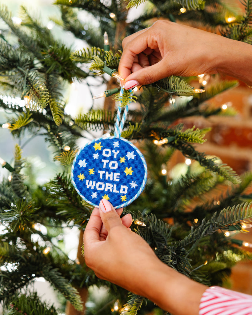 Person hanging a blue ornament with 'Joy to the World' text on a Christmas tree.