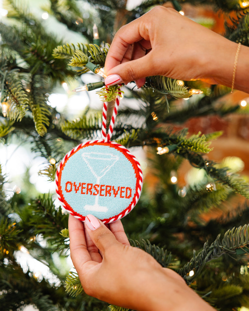 Person hanging a Christmas ornament with 'OVERSERVED' text on a decorated tree.