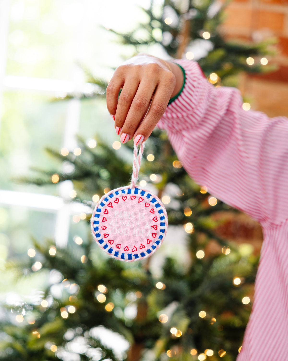 Person holding a Christmas ornament in front of a decorated tree