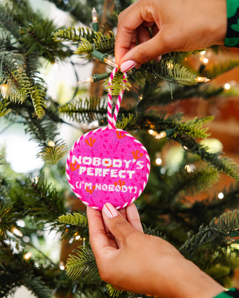 Hand holding a pink ornament with text on a Christmas tree