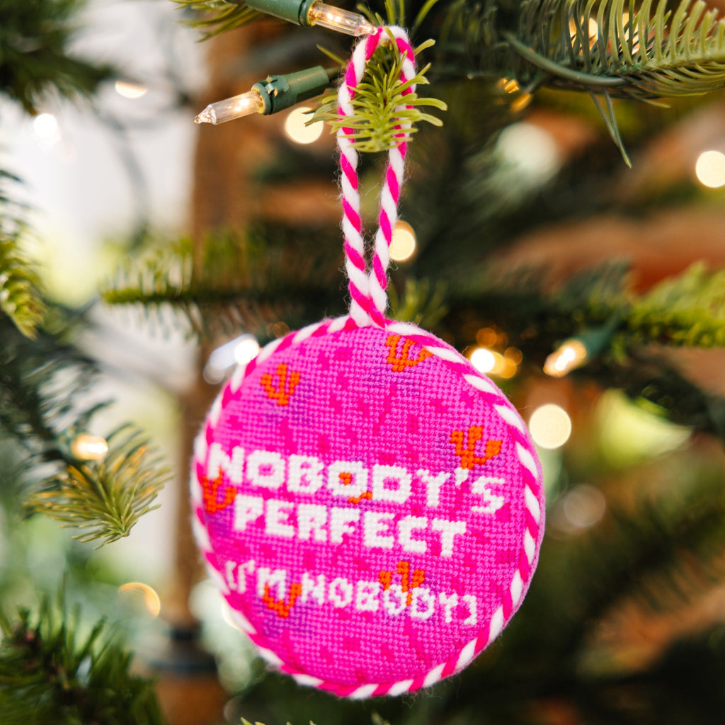 Pink ornament with 'Nobody's Perfect I'm Nobody' text on a Christmas tree.