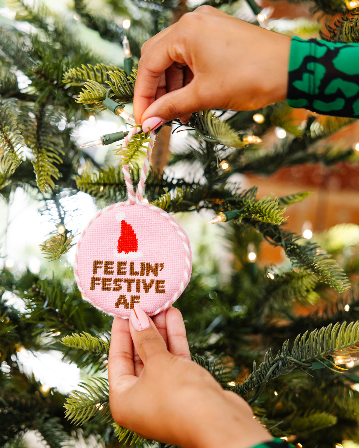 Person hanging a pink ornament with text on a Christmas tree