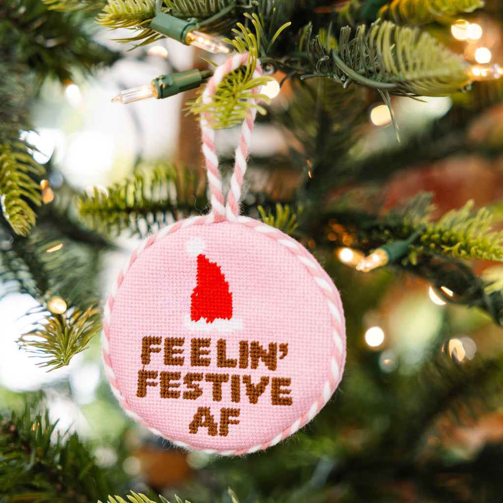 Pink ornament with 'Feelin' Festive AF' text and red tree design on a Christmas tree.