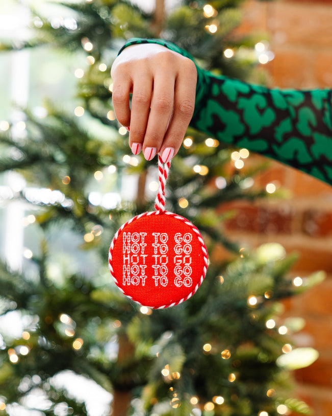 Hand holding a red ornament with text in front of a Christmas tree
