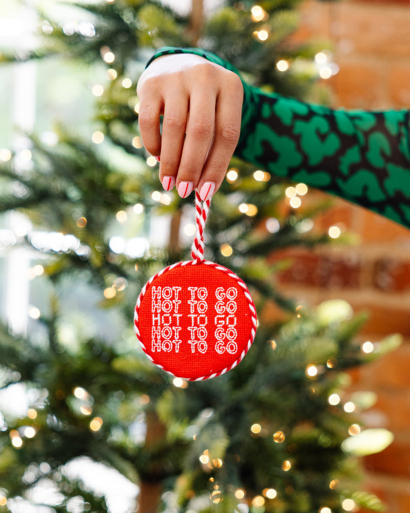 Hand holding a red ornament with text in front of a Christmas tree
