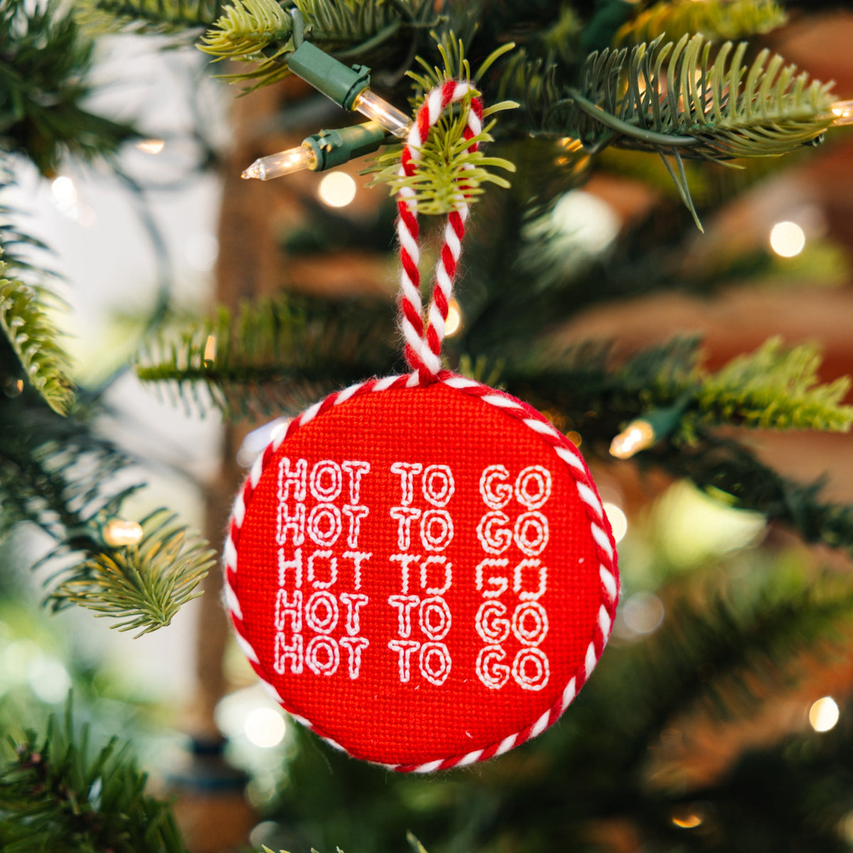 Red ornament with 'Hot to Go' text hanging on a Christmas tree