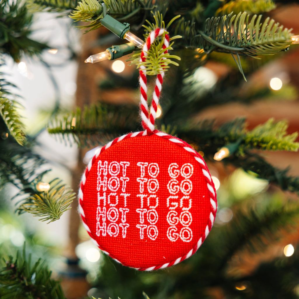 Red ornament with 'Hot to Go' text hanging on a Christmas tree