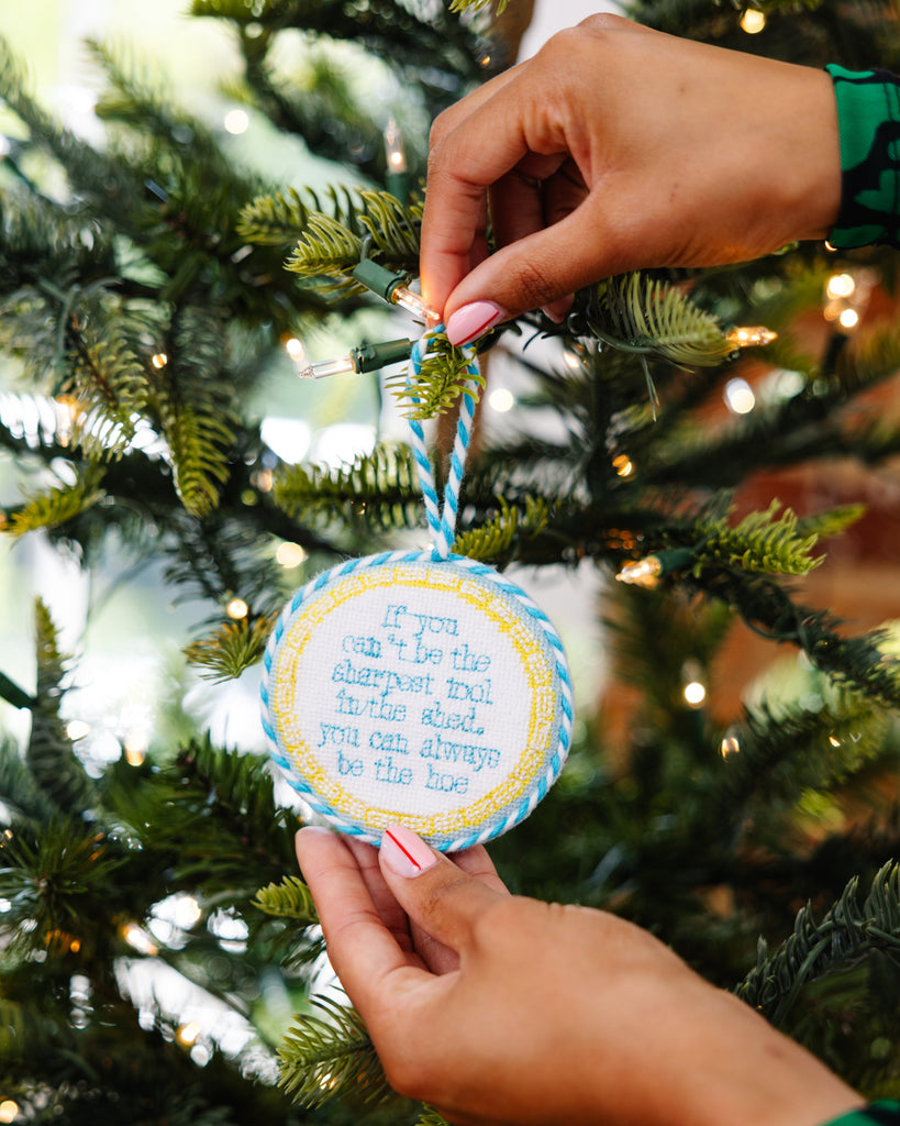 Hand holding a decorative ornament with text on a Christmas tree