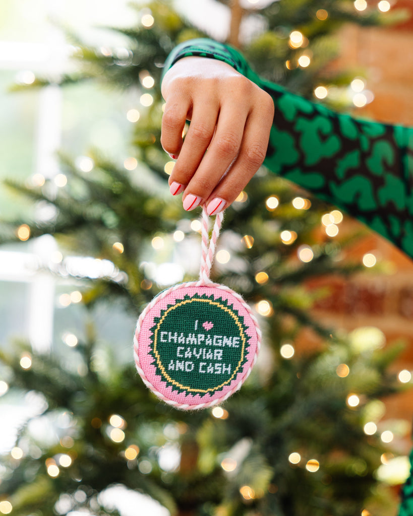 Hand holding a Christmas ornament with text in front of a decorated tree