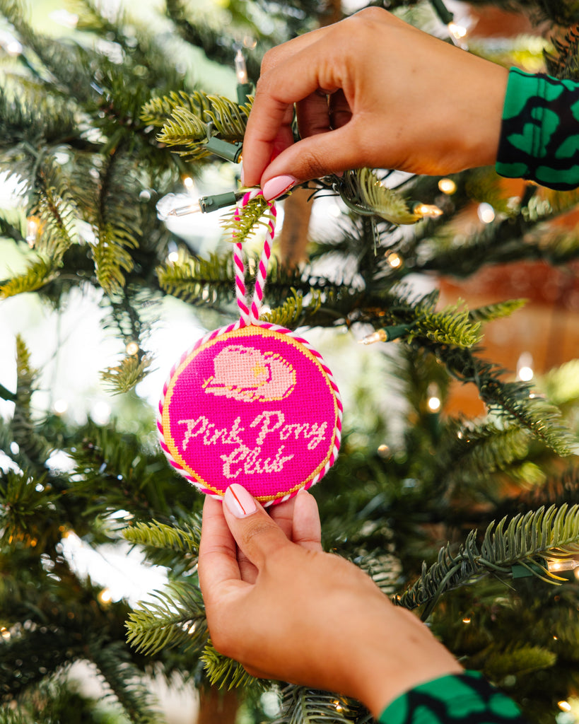 Hand holding a 'Pink Pony Club' ornament on a Christmas tree