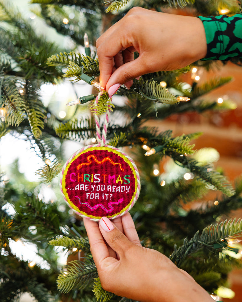 Hand holding a Christmas ornament with text against a decorated tree background