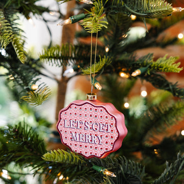Pink ornament with 'Let's Get Merry' text on a Christmas tree