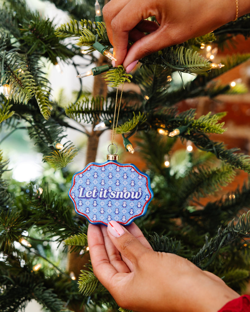 Person decorating a Christmas tree with a 'Let it snow' ornament.