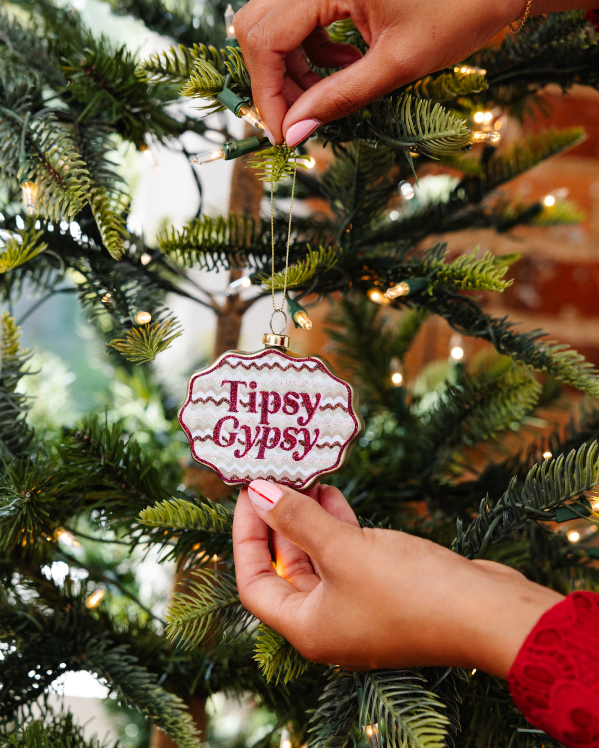 Hand holding a 'Tipsy Gypsy' ornament on a Christmas tree.