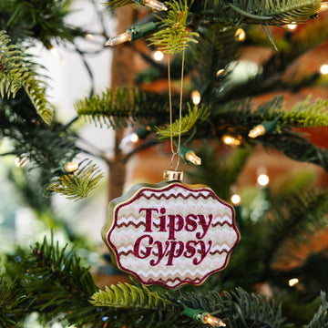 Ornament with 'Tipsy Gypsy' text hanging on a Christmas tree.