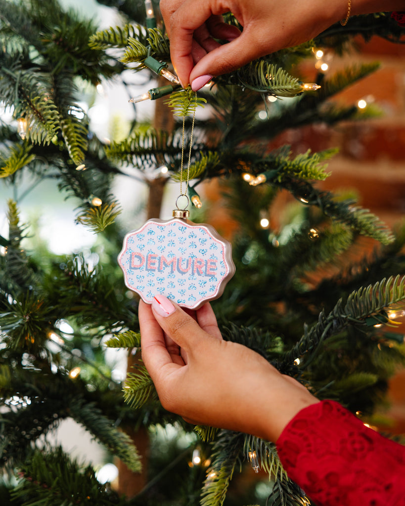Person decorating a Christmas tree with a 'DEMIUR' ornament.