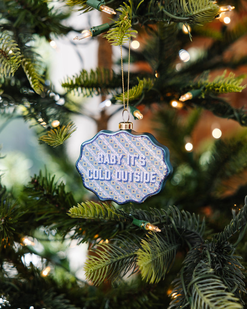 Decorative ornament with 'Baby it's cold outside' text on a Christmas tree.