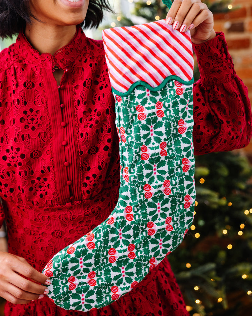 Woman holding a Christmas stocking with a festive design in front of a decorated Christmas tree.