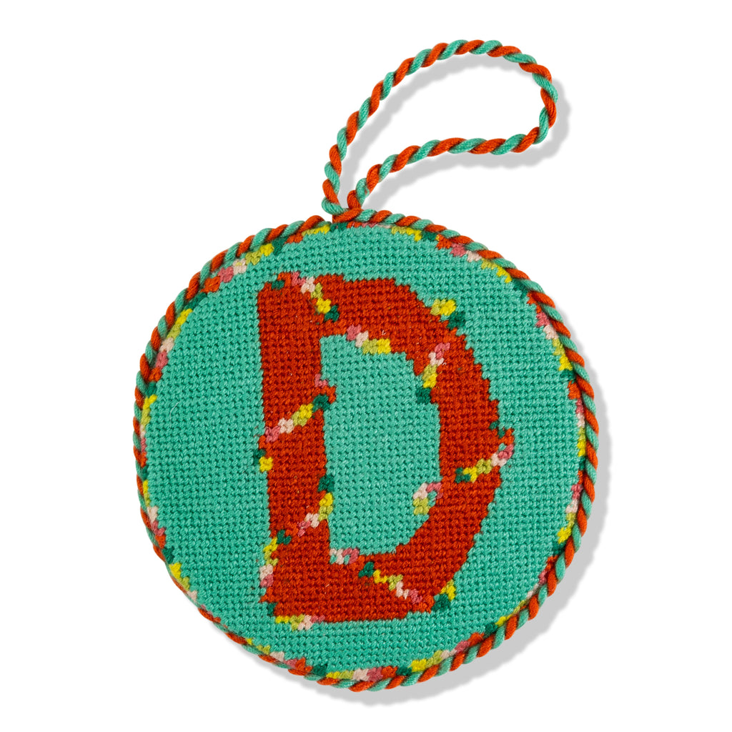 Circular needlepoint ornament with letter 'D' on a turquoise background