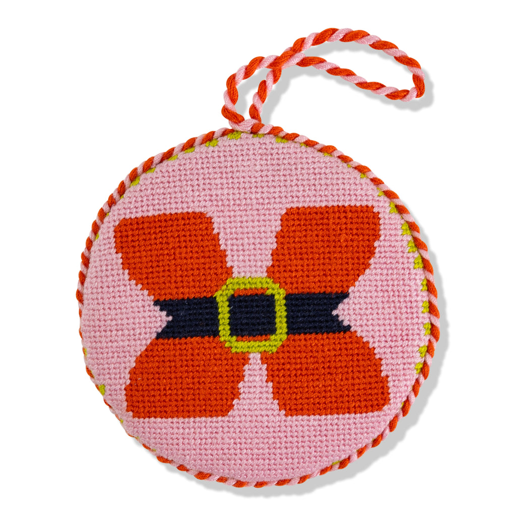 Circular needlepoint ornament with a red flower design on a pink background, hanging by a red and white string.