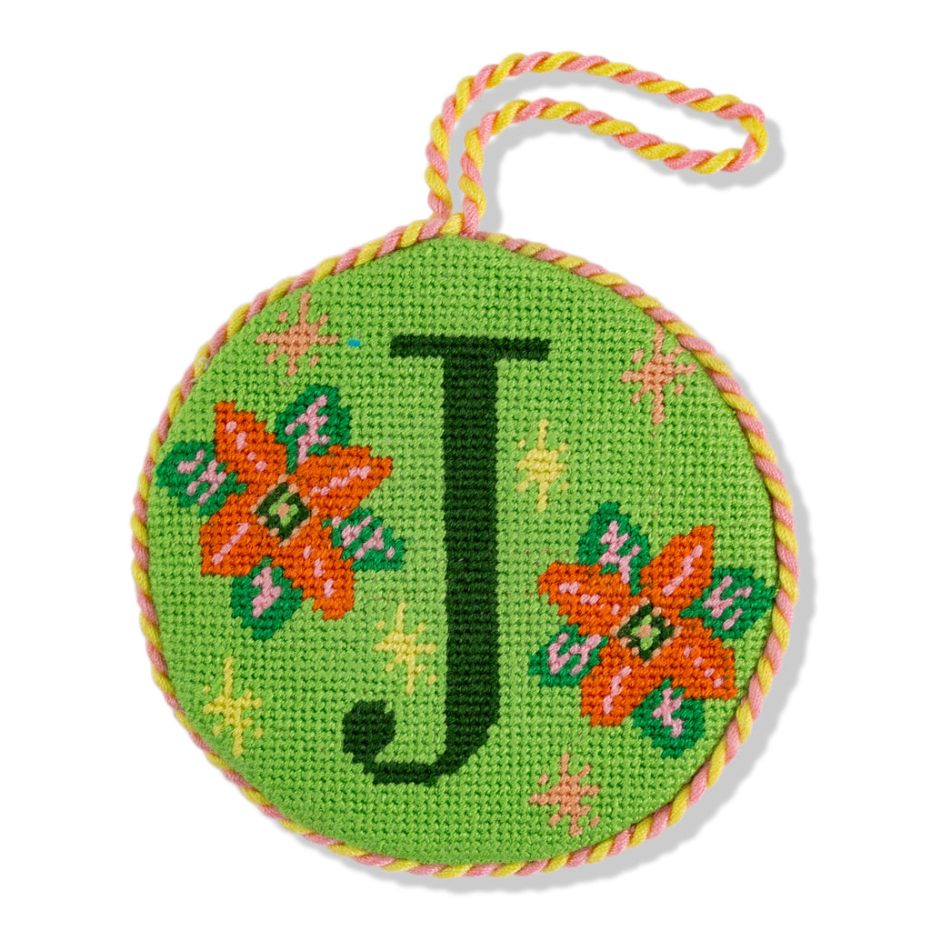 Circular green needlepoint ornament with letter 'J' and floral designs on a white background