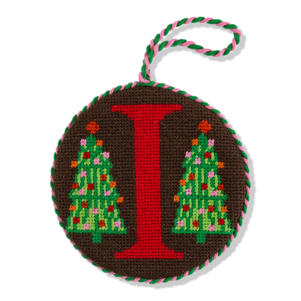 Decorative ornament with letter 'I' and Christmas tree design on a brown background.