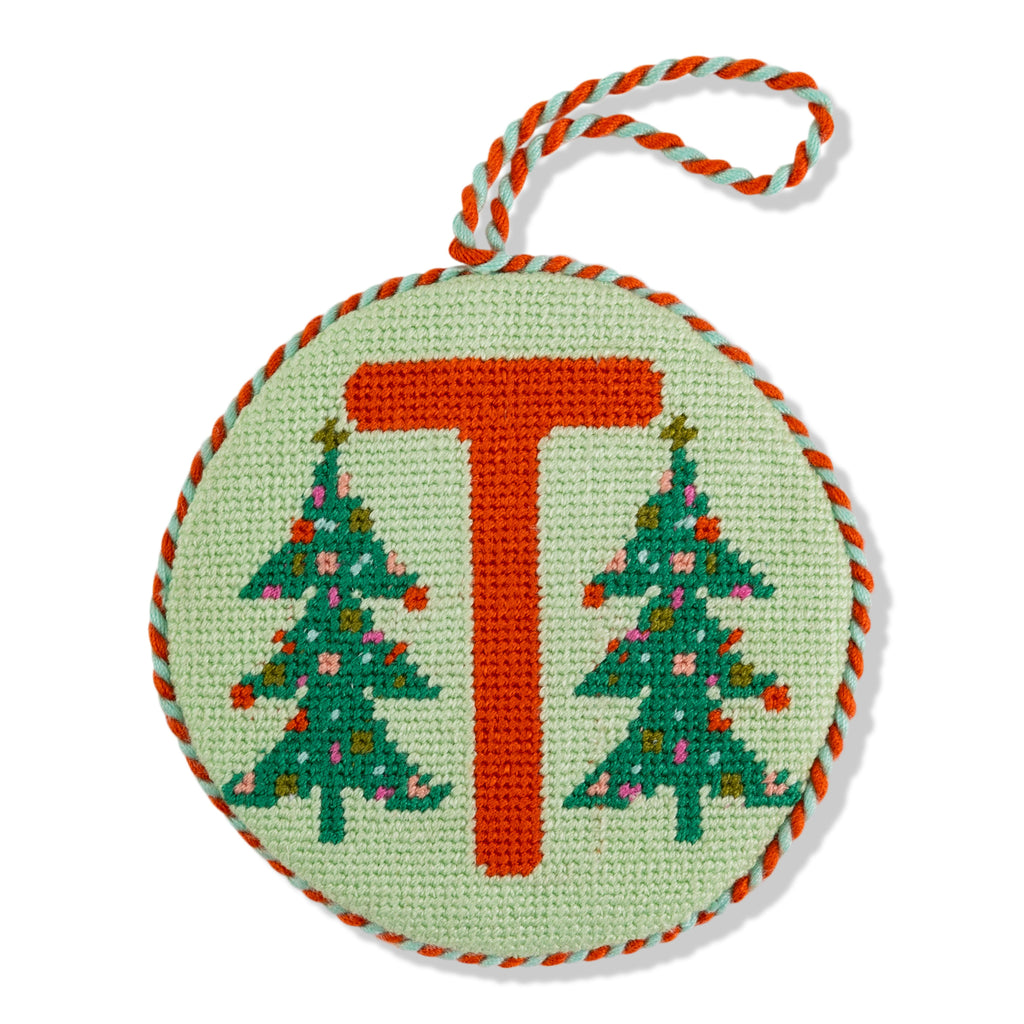 Circular needlepoint ornament with letter 'T' and Christmas trees on a light green background.