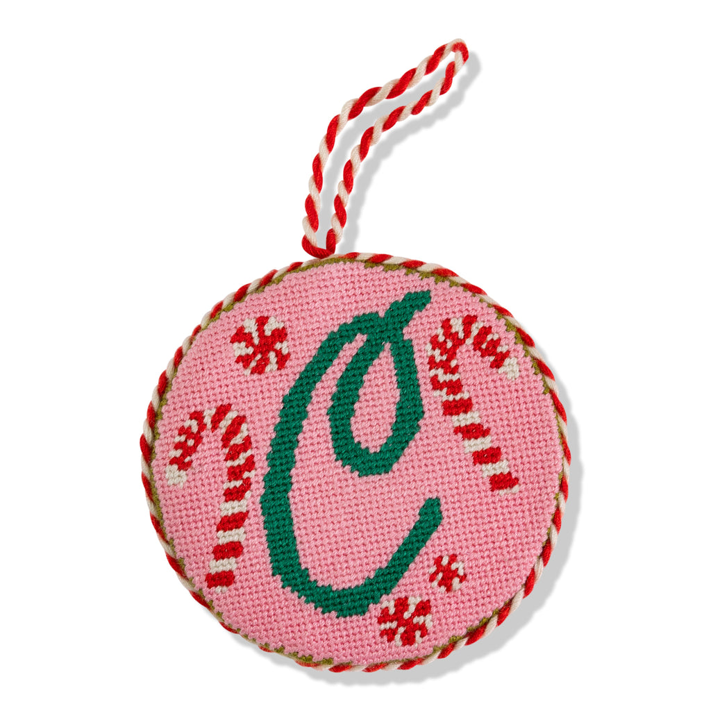 Decorative ornament with letter 'C' on a pink background with red snowflakes and green candy canes, attached to red and white string.