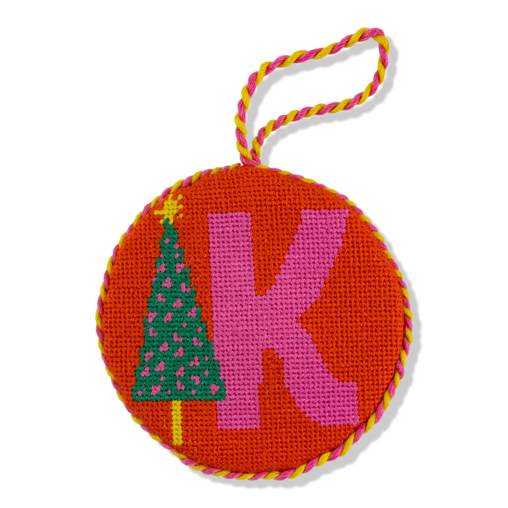 Round needlepoint ornament with letter 'K' and Christmas tree design on orange background