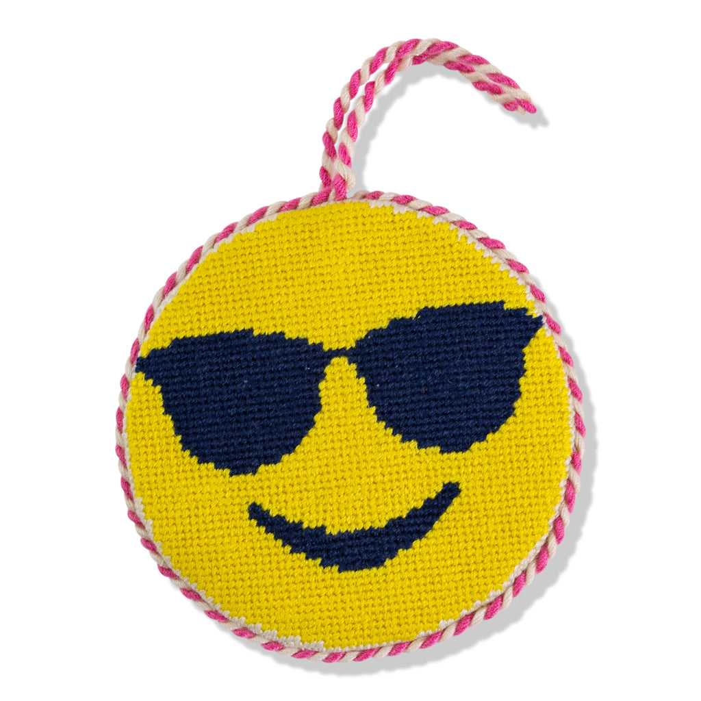 Round yellow toy with smiley face and sunglasses design, pink and white rope handle on a white background