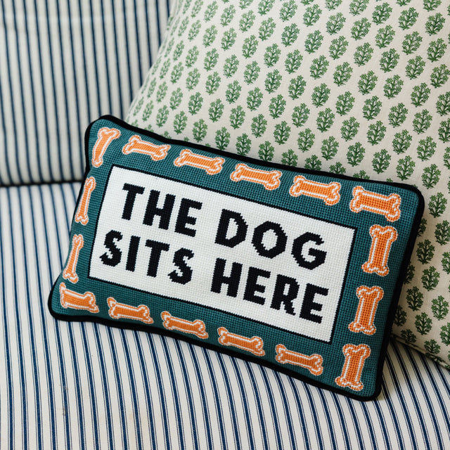 Decorative pillow with 'The Dog Sits Here' text on a striped sofa.