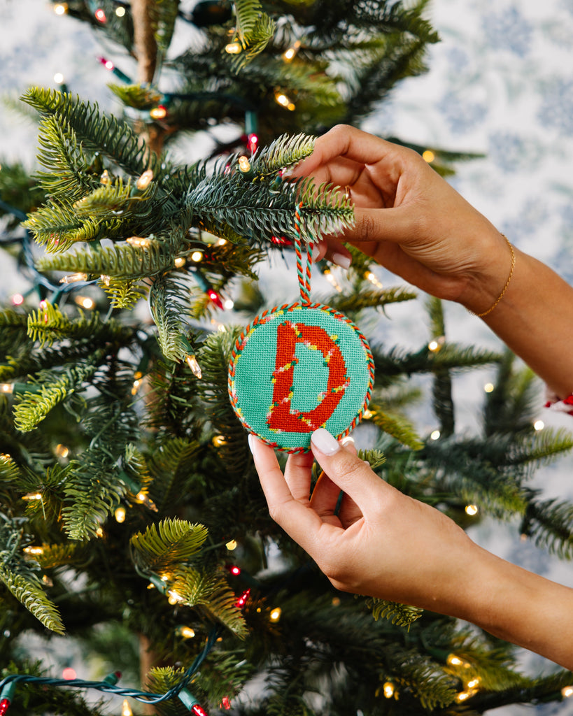 Hand placing a decorative ornament with a letter 'D' on a Christmas tree.