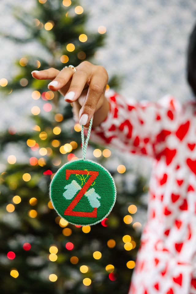 Hand holding a green ornament with a letter 'Z' in front of a decorated Christmas tree.
