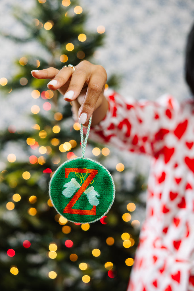 Hand holding a green ornament with a letter 'Z' in front of a decorated Christmas tree.