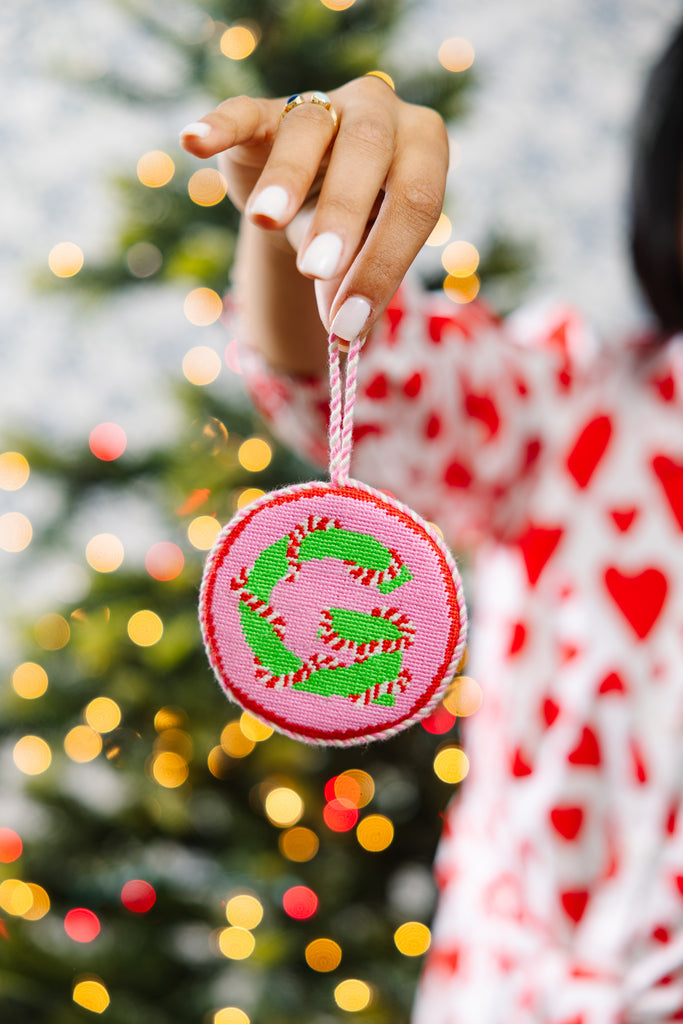 Person holding a Christmas ornament with a tree and lights in the background