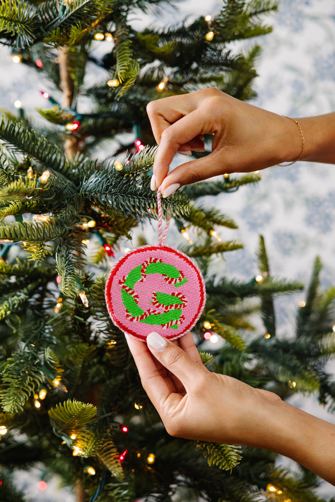Hand placing a pink and green ornament on a Christmas tree.