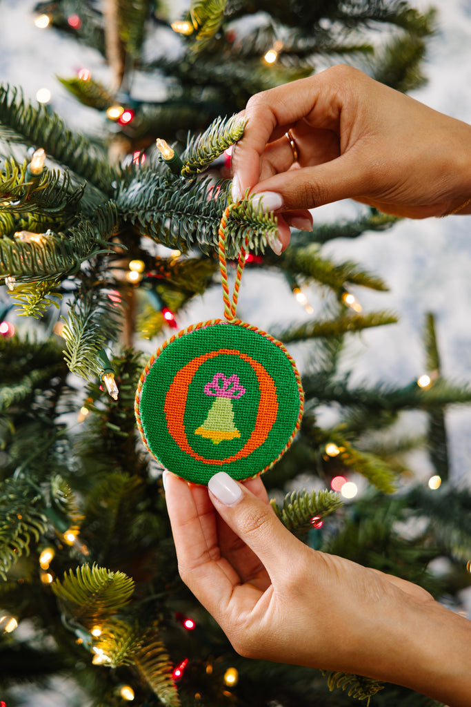 Hand holding a decorative ornament with a Christmas tree in the background