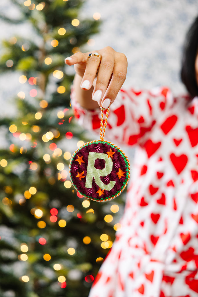 Person holding a Christmas ornament with a letter 'R' in front of a decorated tree.
