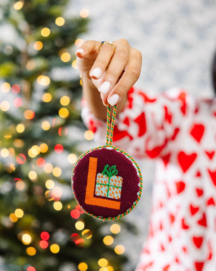 Person holding a Christmas ornament with a tree and gift design in front of a decorated Christmas tree.