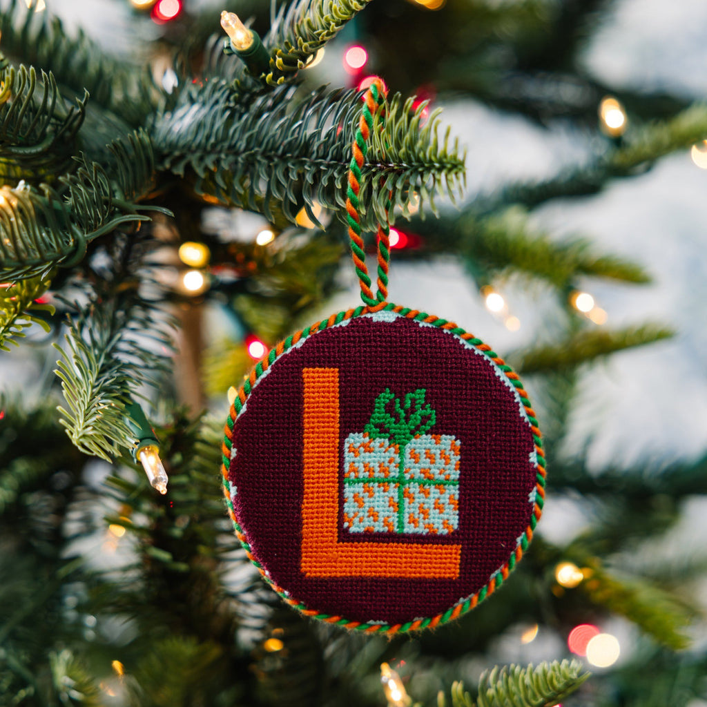 Decorative Christmas ornament with letter 'L' on a tree with lights in the background