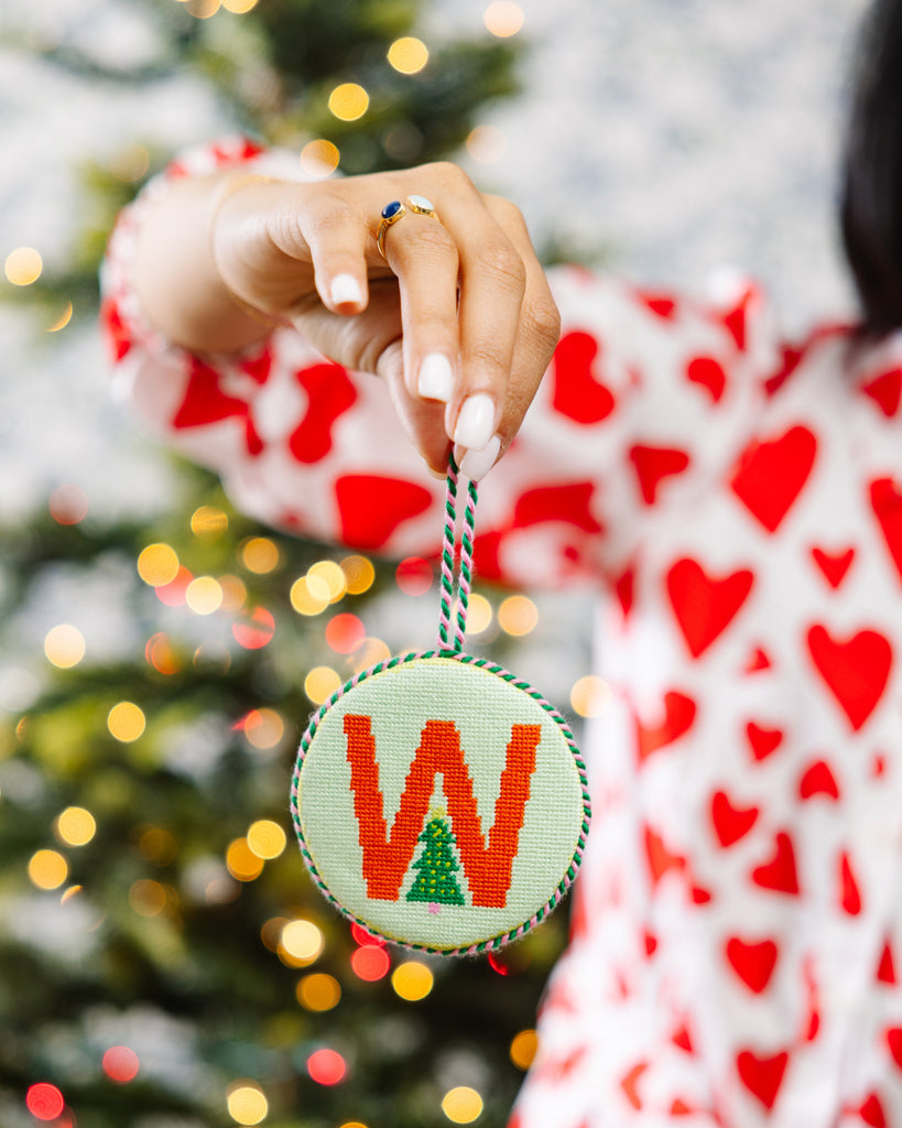 Person holding a Christmas ornament with a letter 'W' in front of a decorated tree.