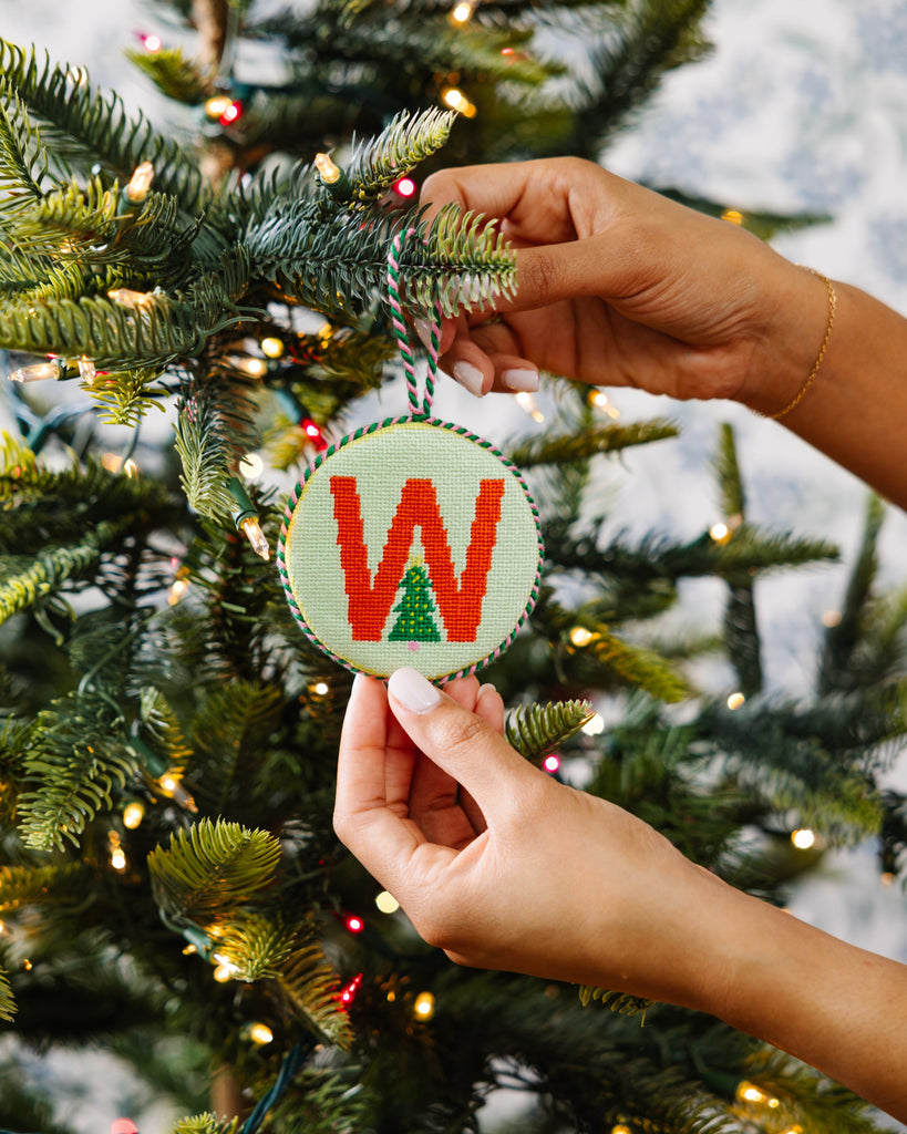Person holding a Christmas ornament with 'W' on a decorated tree