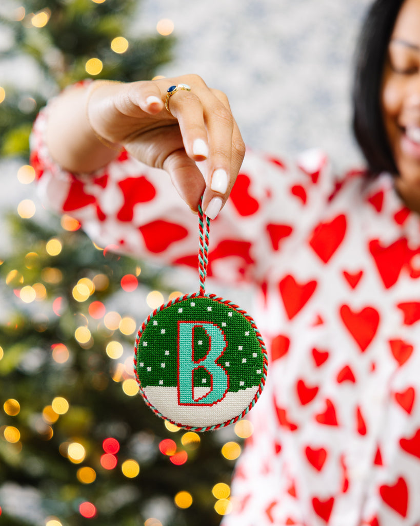 Person holding a Christmas ornament with a letter 'B' in front of a decorated tree.