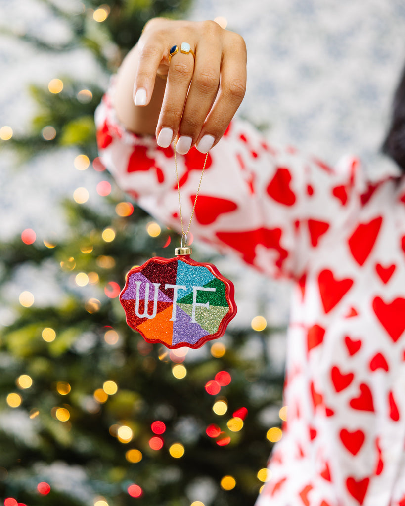 Person holding a colorful ornament in front of a Christmas tree with lights.