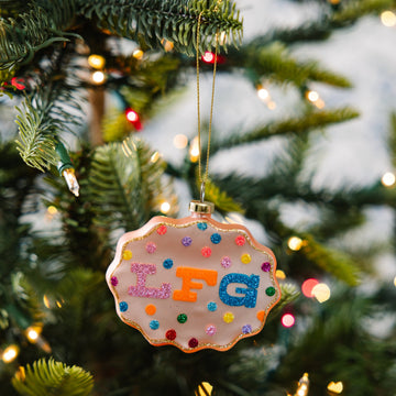 Decorative ornament with colorful text hanging on a Christmas tree.